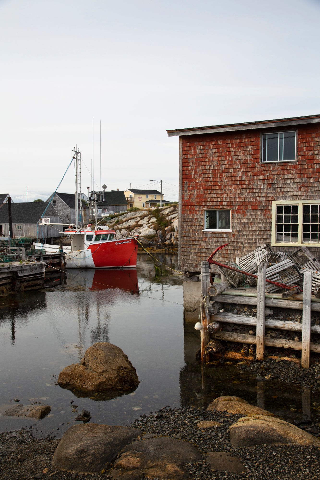 Red fishing boat moored beside a rustic brick building in a quiet coastal harbor.