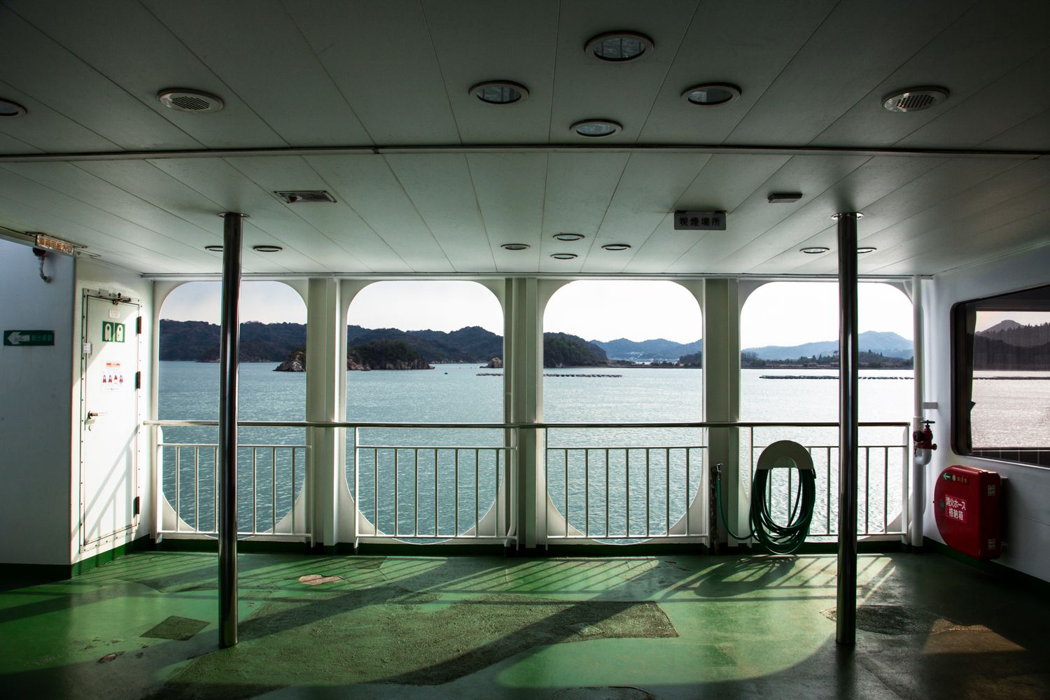 Interior view of an empty ferry cabin with windows overlooking water and mountains.