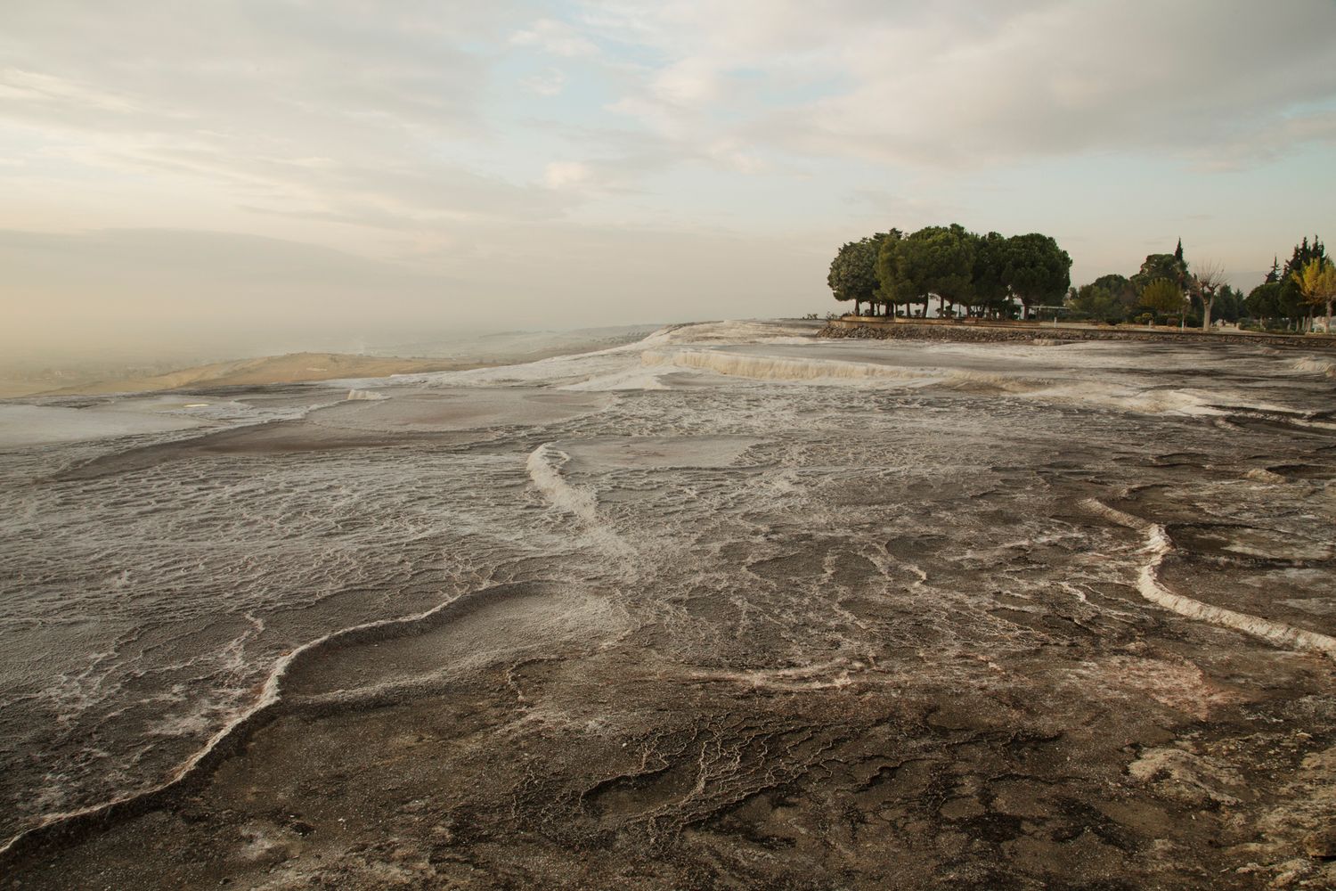 Natural limestone terraces with flowing water patterns stretching towards distant trees.