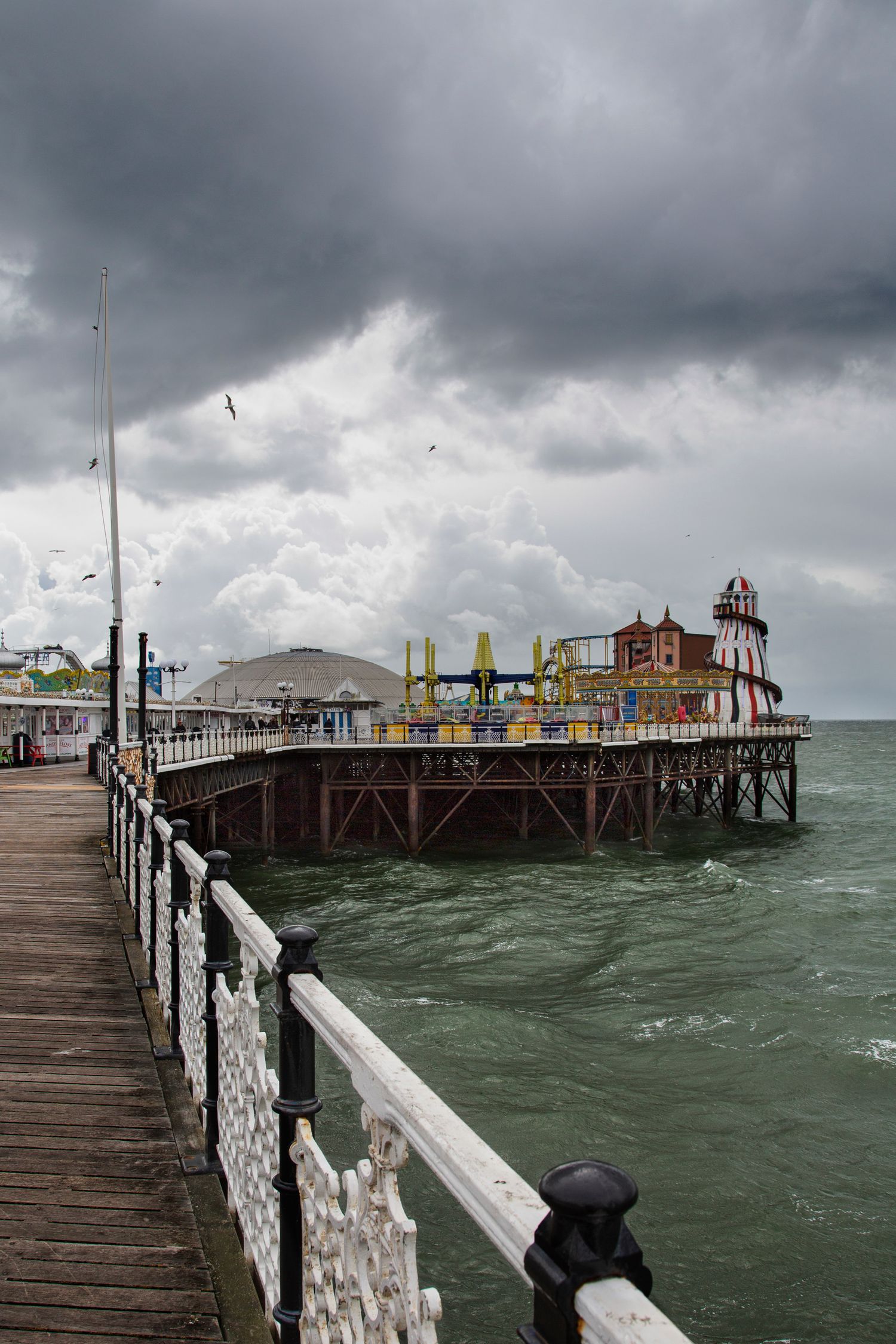 Stormy skies over Brighton Pier with rough seas and wooden boardwalk.