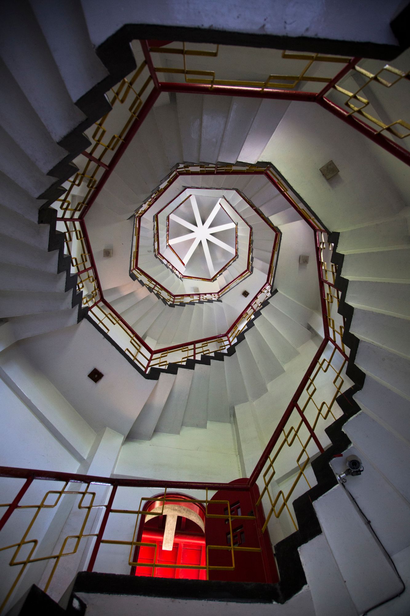 Spiraling white staircase with red handrails viewed from below creates a geometric pattern.