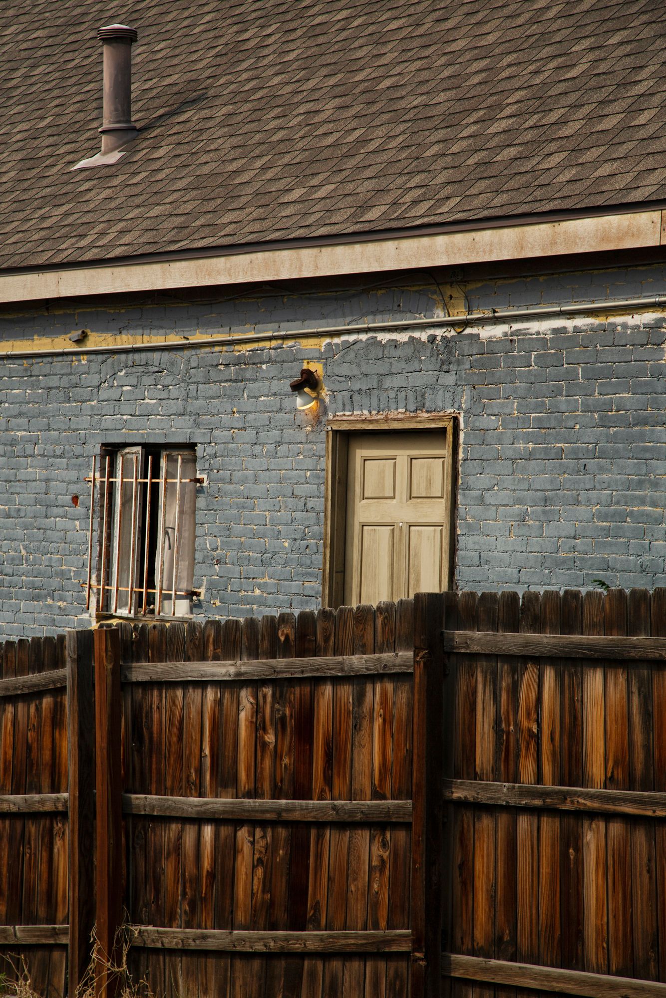Weathered wooden fence with peeling blue paint and multiple doors along a residential building exterior.