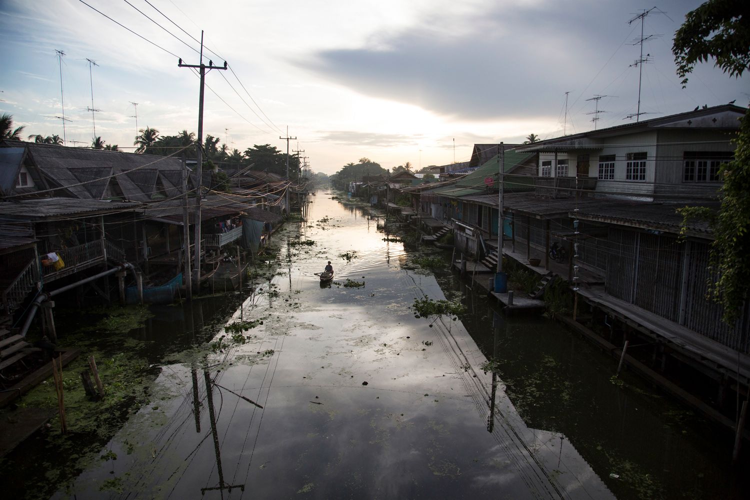 Flooded urban street with power lines and buildings reflecting in still waters at dusk.