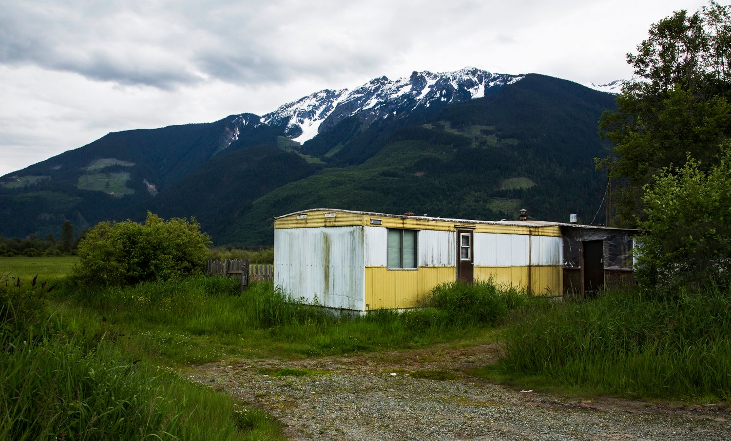 Yellow and blue trailer sits in grassy field with snow-capped mountain peak in background.