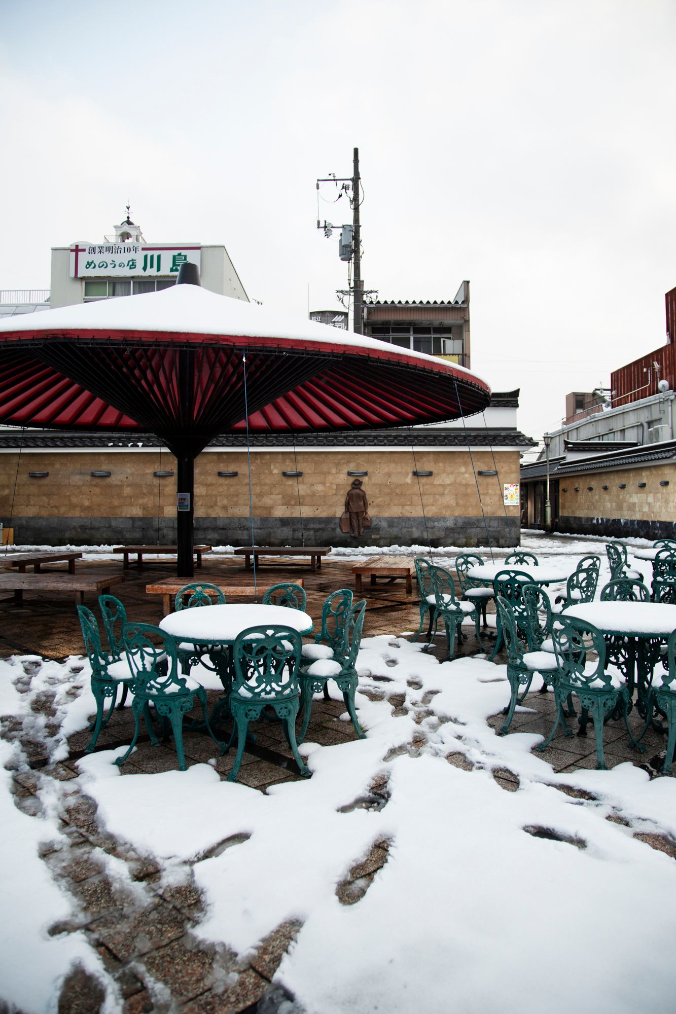Snow covered outdoor seating area with red umbrellas and turquoise chairs.