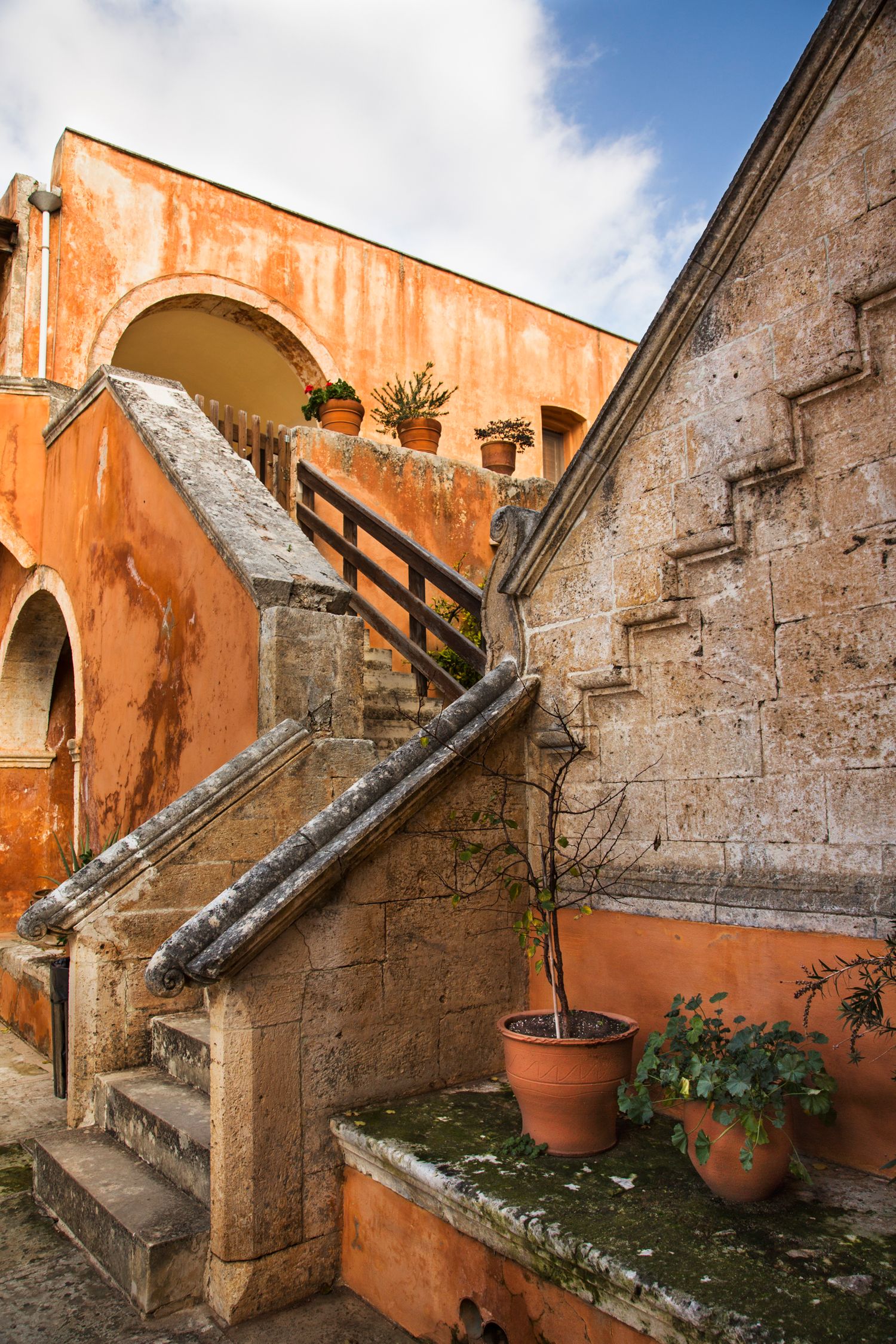Ancient stone stairs and weathered orange walls create a Mediterranean architectural atmosphere in a historic courtyard.