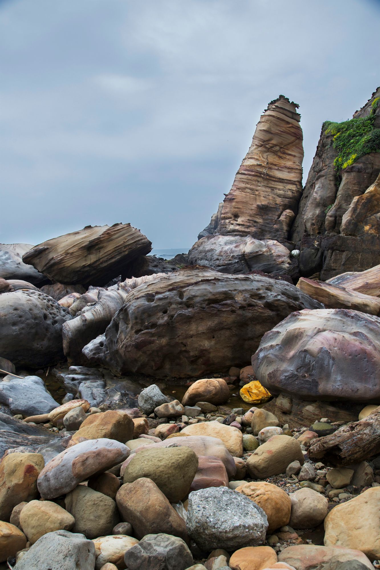 Rocky coastal landscape with smooth boulders and rugged cliffs against blue sky.