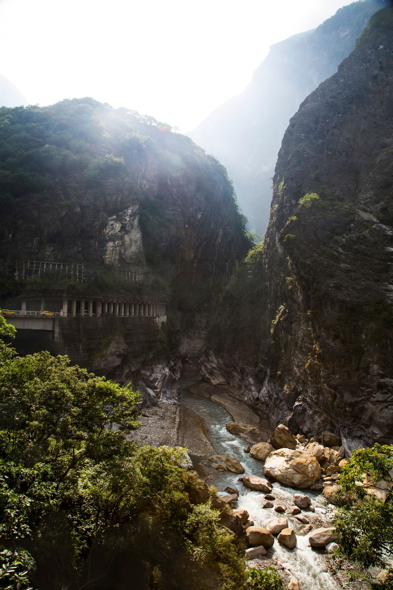 Misty mountain gorge with rushing river and steep rocky cliffs in dramatic lighting.