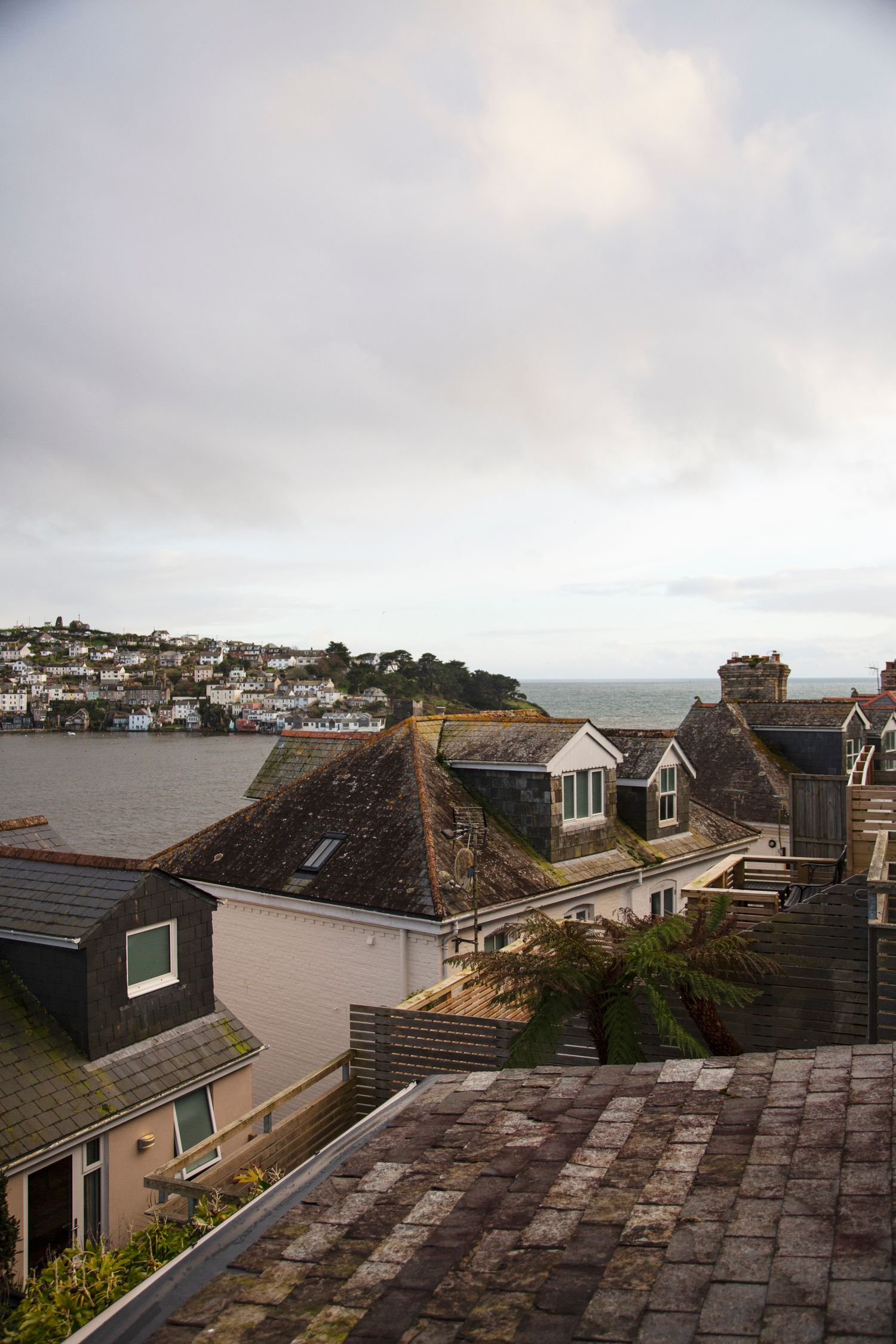 Rooftop view of coastal houses overlooking a harbor town under cloudy skies.