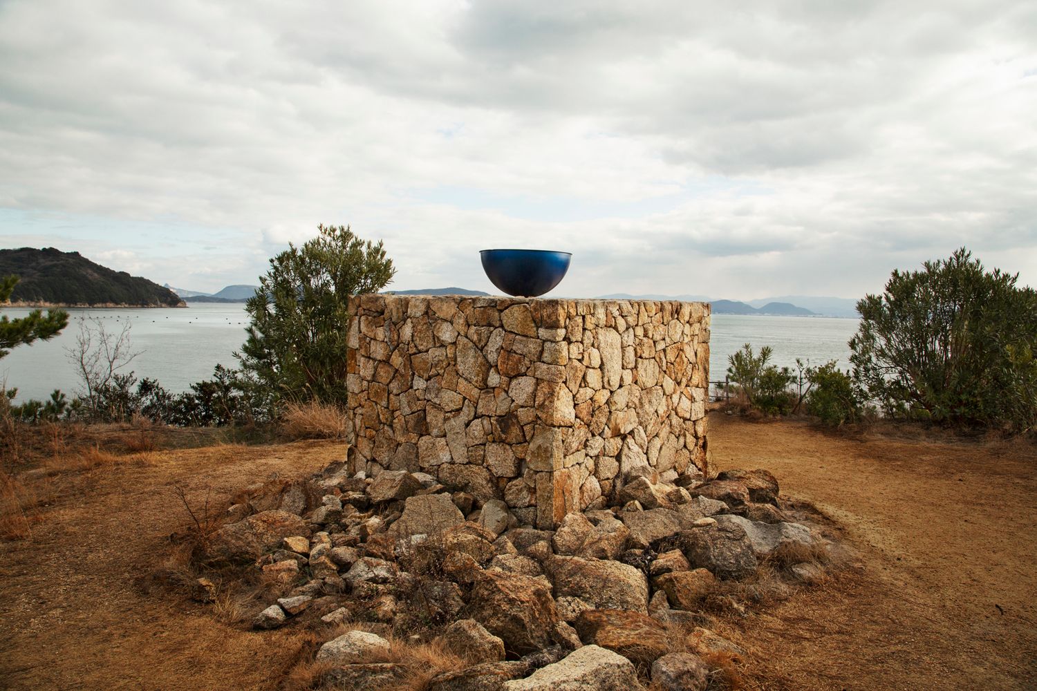 Ancient stone ruins sit atop a cliff overlooking a scenic coastal landscape at sunset.