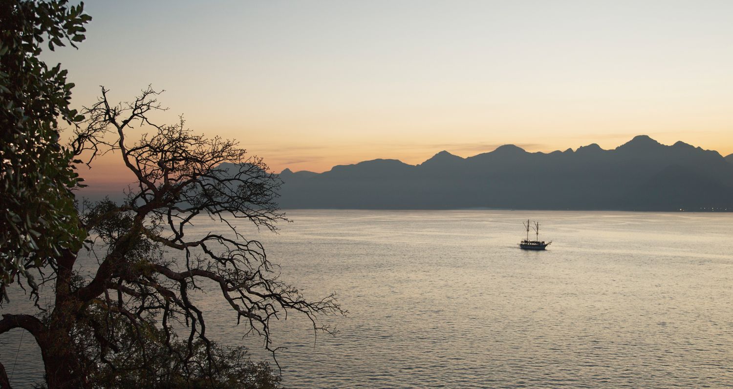 Tranquil sunset seascape with mountain silhouettes and sailboat on calm waters.