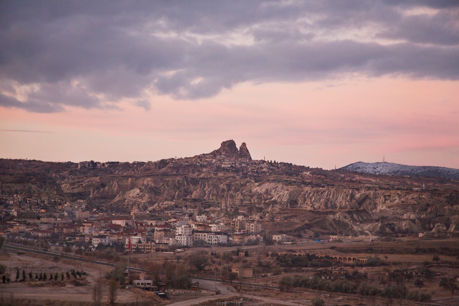 Rugged mountain town nestled among rocky terrain at sunset with dramatic cloudy sky.