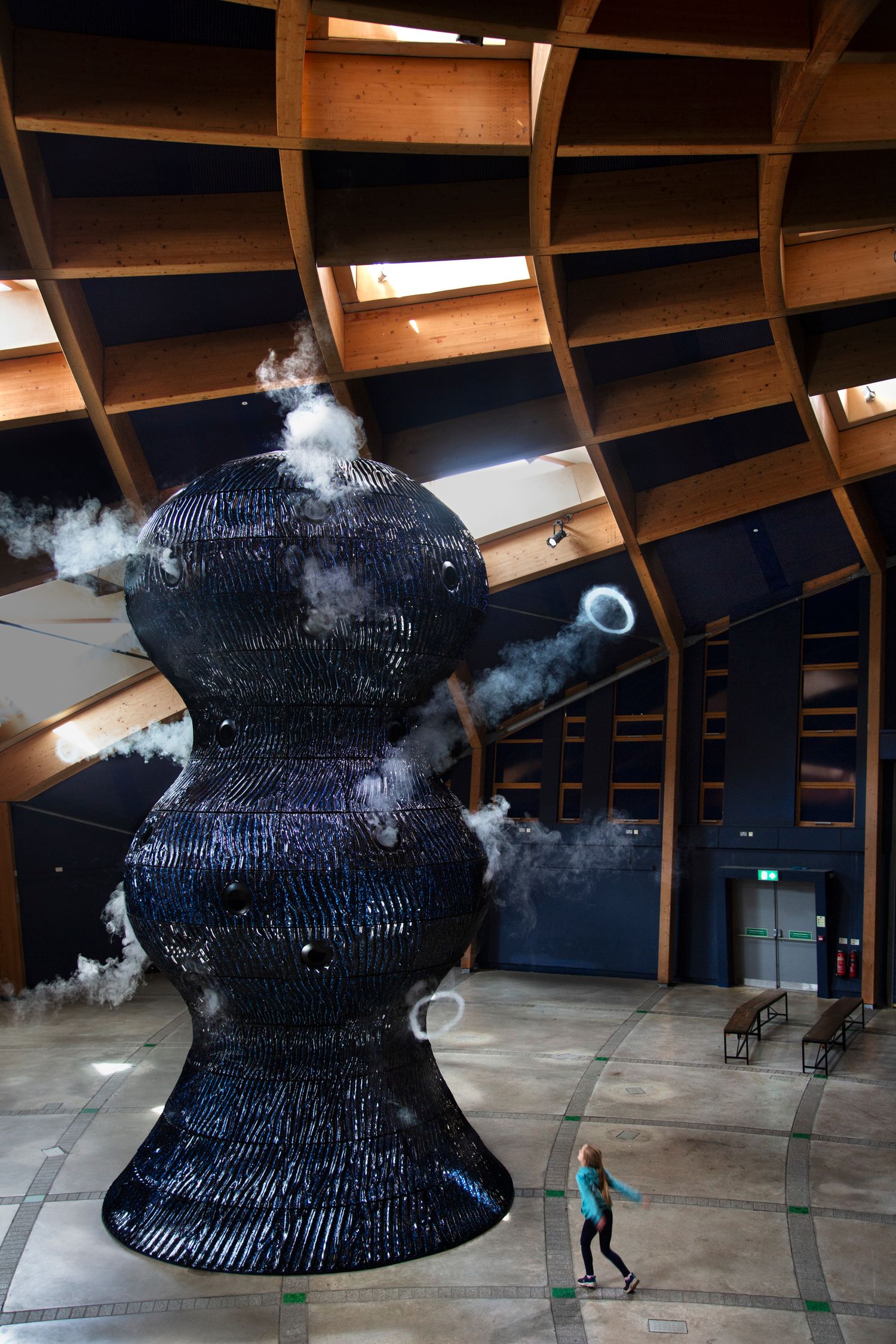 Modern architectural space featuring a large dark sculptural installation with dramatic lighting.