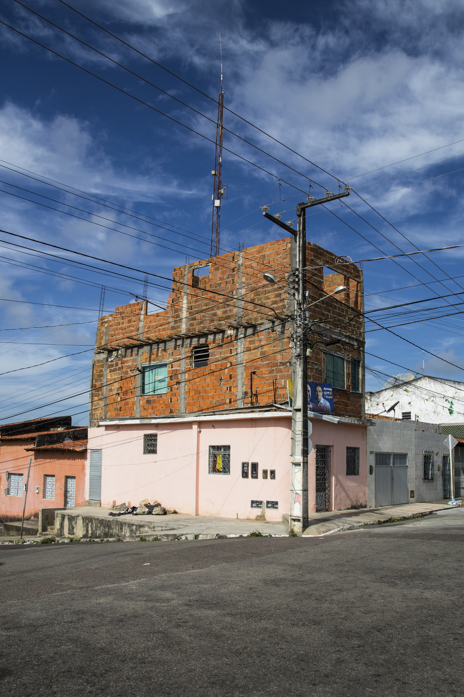 Unfinished brick construction on top of pink building with power lines against blue sky.