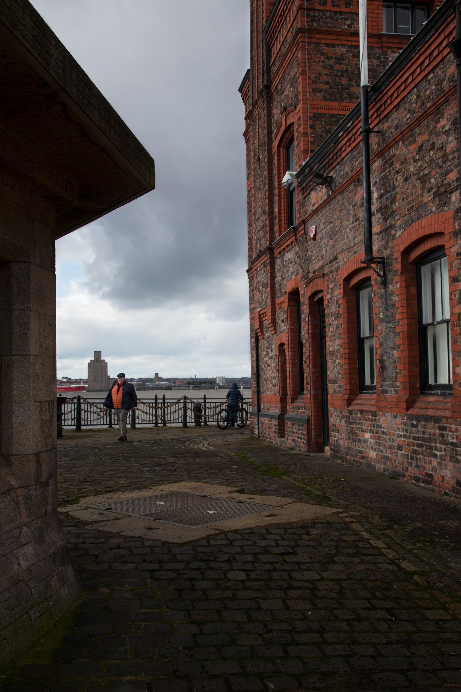 Red brick industrial building with cobblestone pathway and cloudy sky in the background.