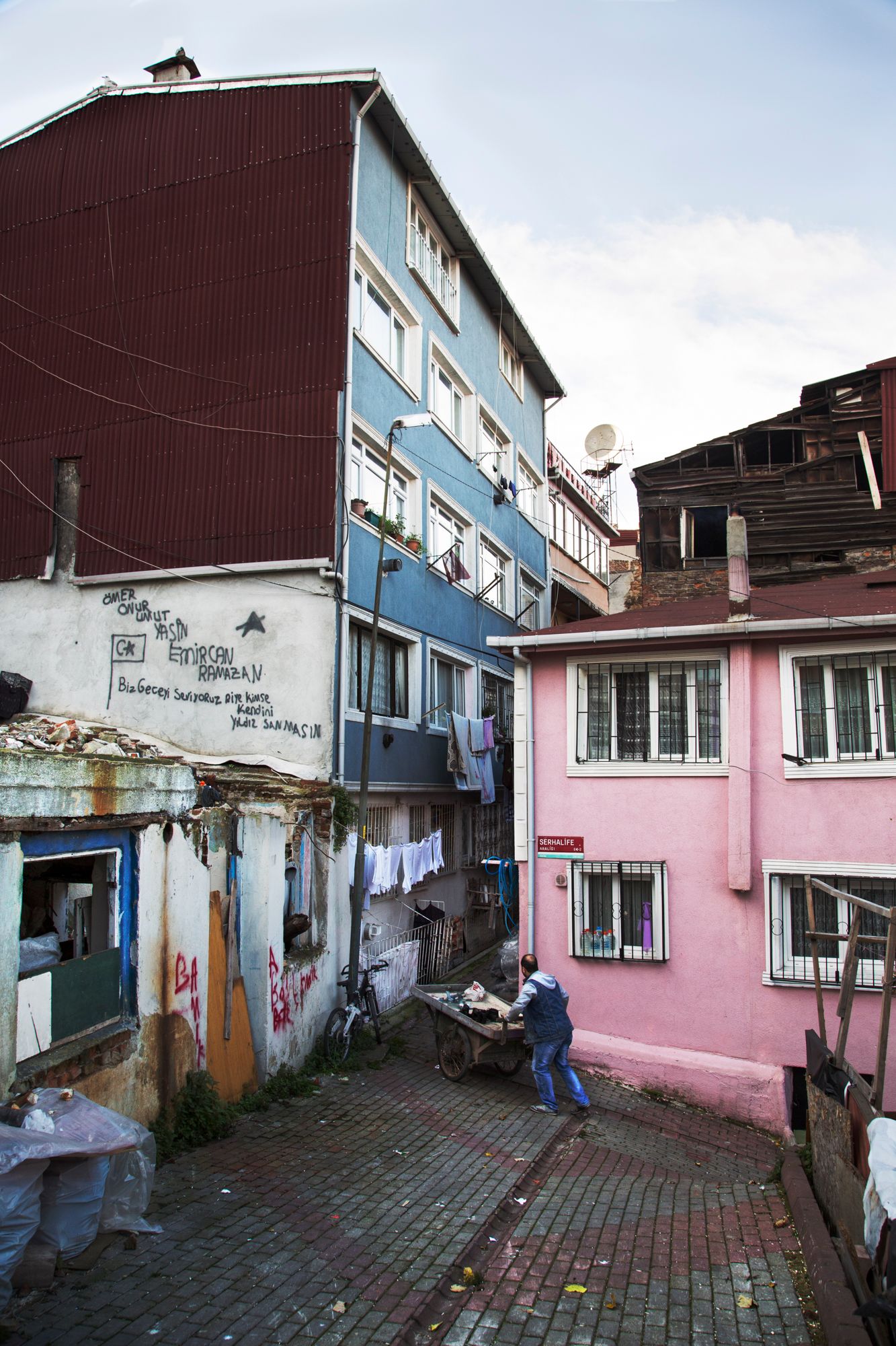 Pink apartment building exterior with hanging laundry and graffiti on weathered walls in urban setting.
