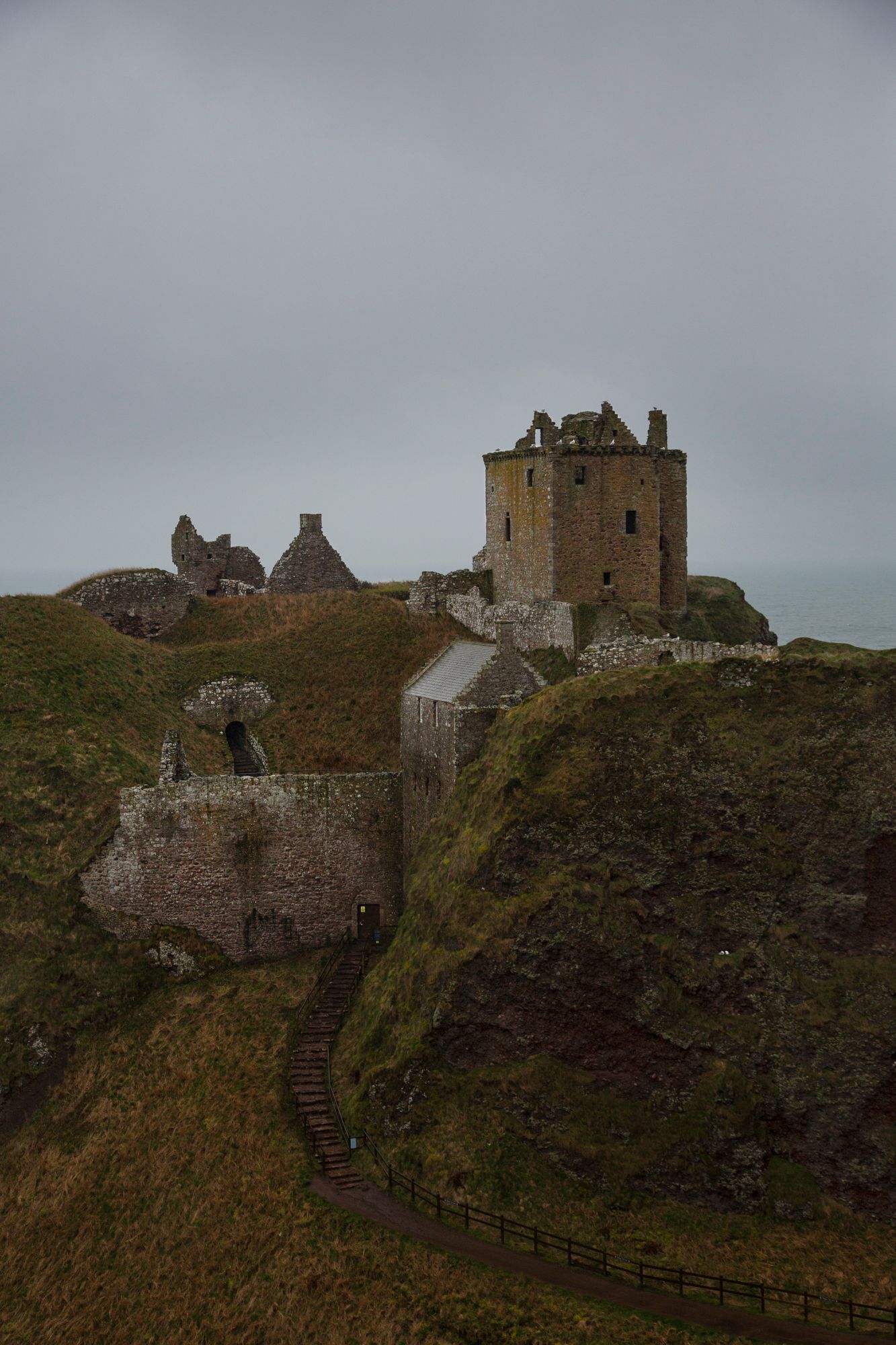 Ancient stone castle ruins perched dramatically on misty cliffs along the Scottish coastline at Dunnottar Castle.