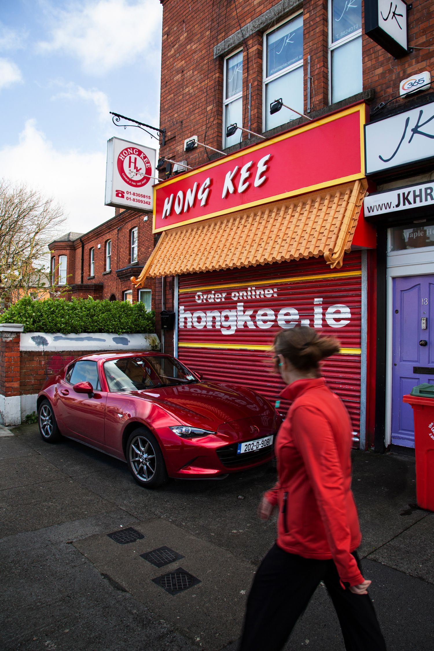 Red brick storefront of Hong Kee restaurant with red sports car parked outside.