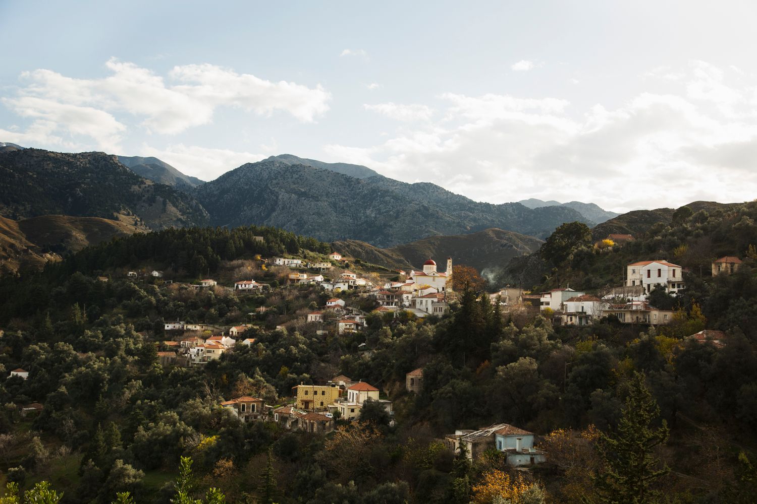 Panoramic view of hillside residential area nestled among lush mountains with Mediterranean architecture.