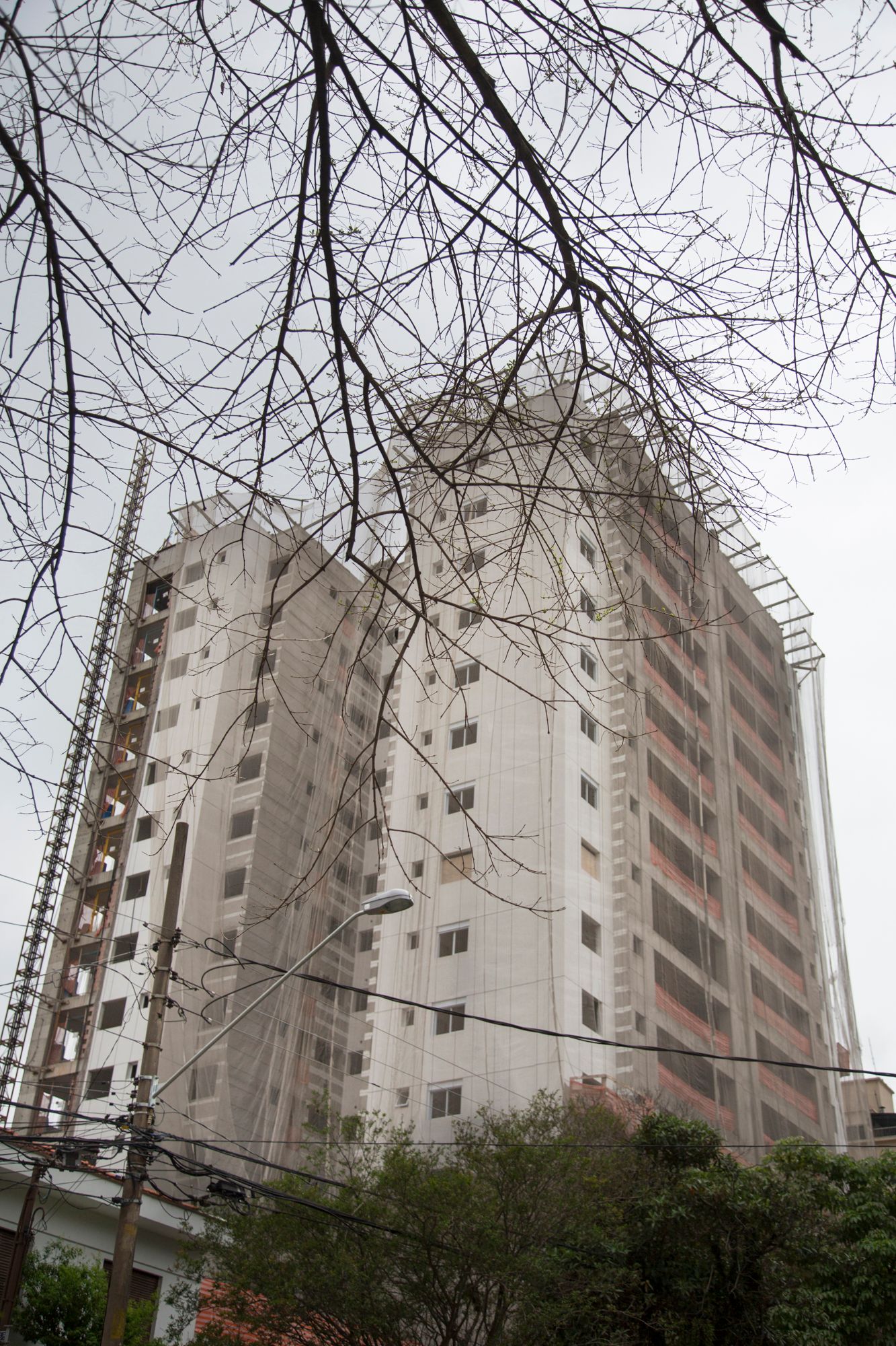 Tall apartment buildings viewed through bare tree branches against an overcast sky.