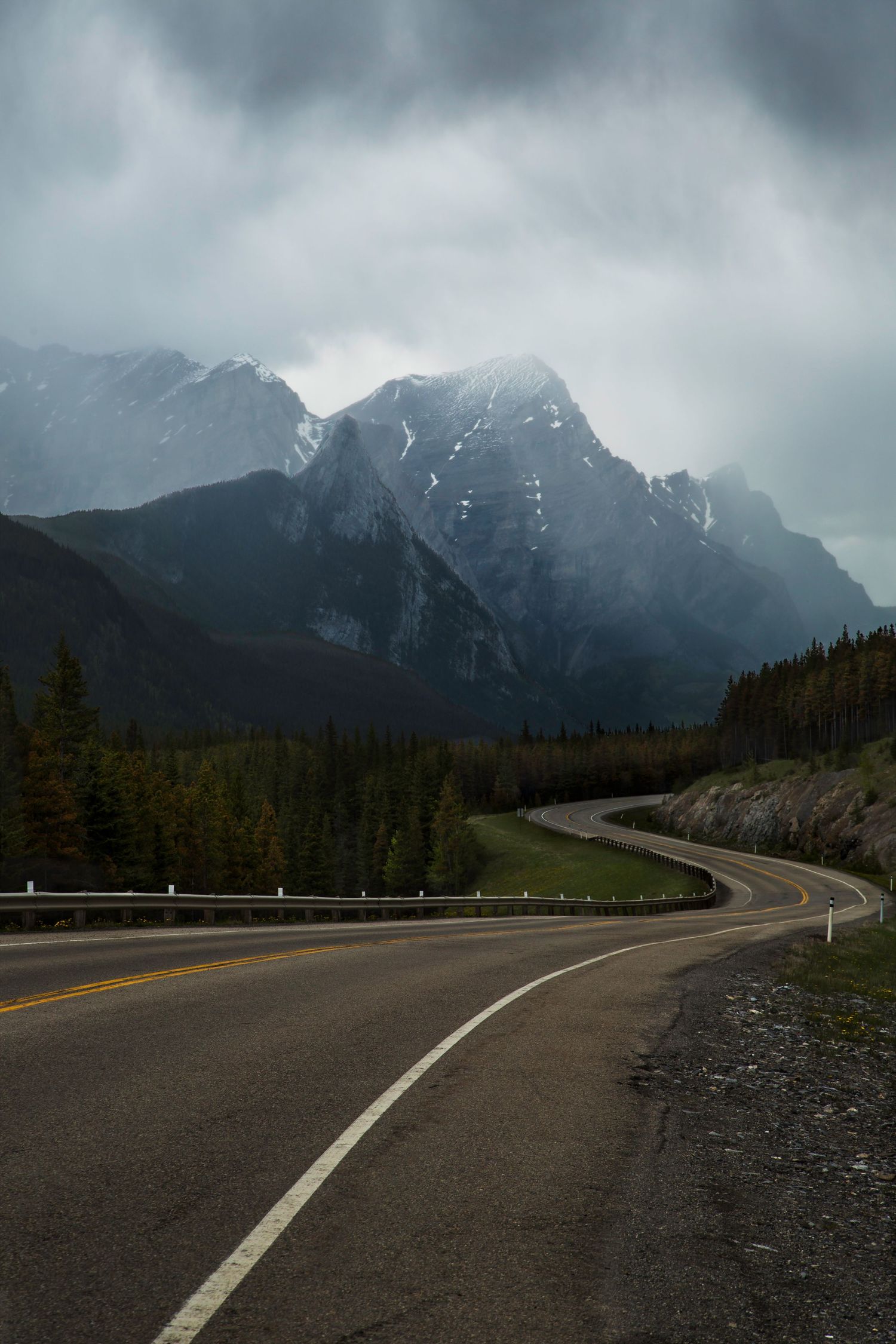 Winding mountain highway leads toward misty snow-capped peaks in dramatic landscape.