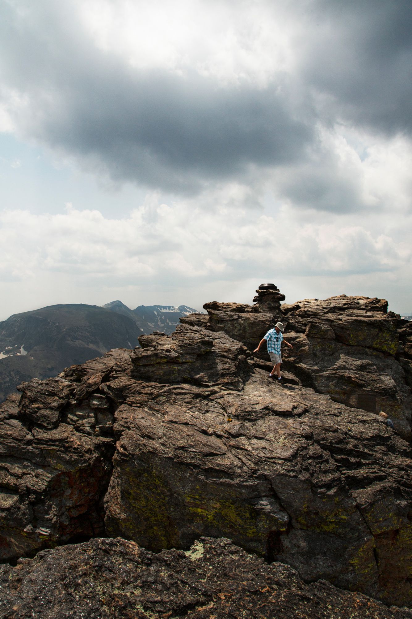 Dramatic panoramic view of rocky mountain cliffs under stormy clouds with a small figure visible on the ridge.