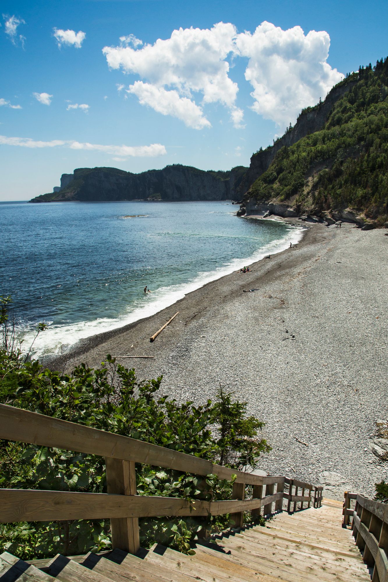 Scenic pebble beach with wooden stairs leading down to pristine shoreline surrounded by forested cliffs.