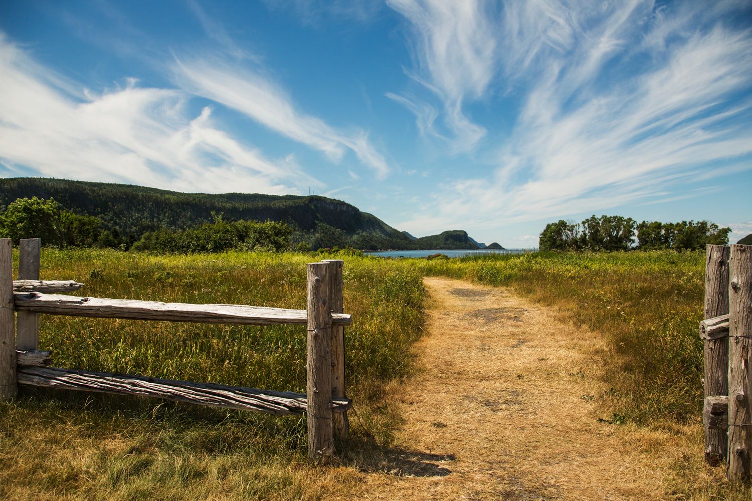 Rustic wooden fence along grassy trail with mountains in the distance.