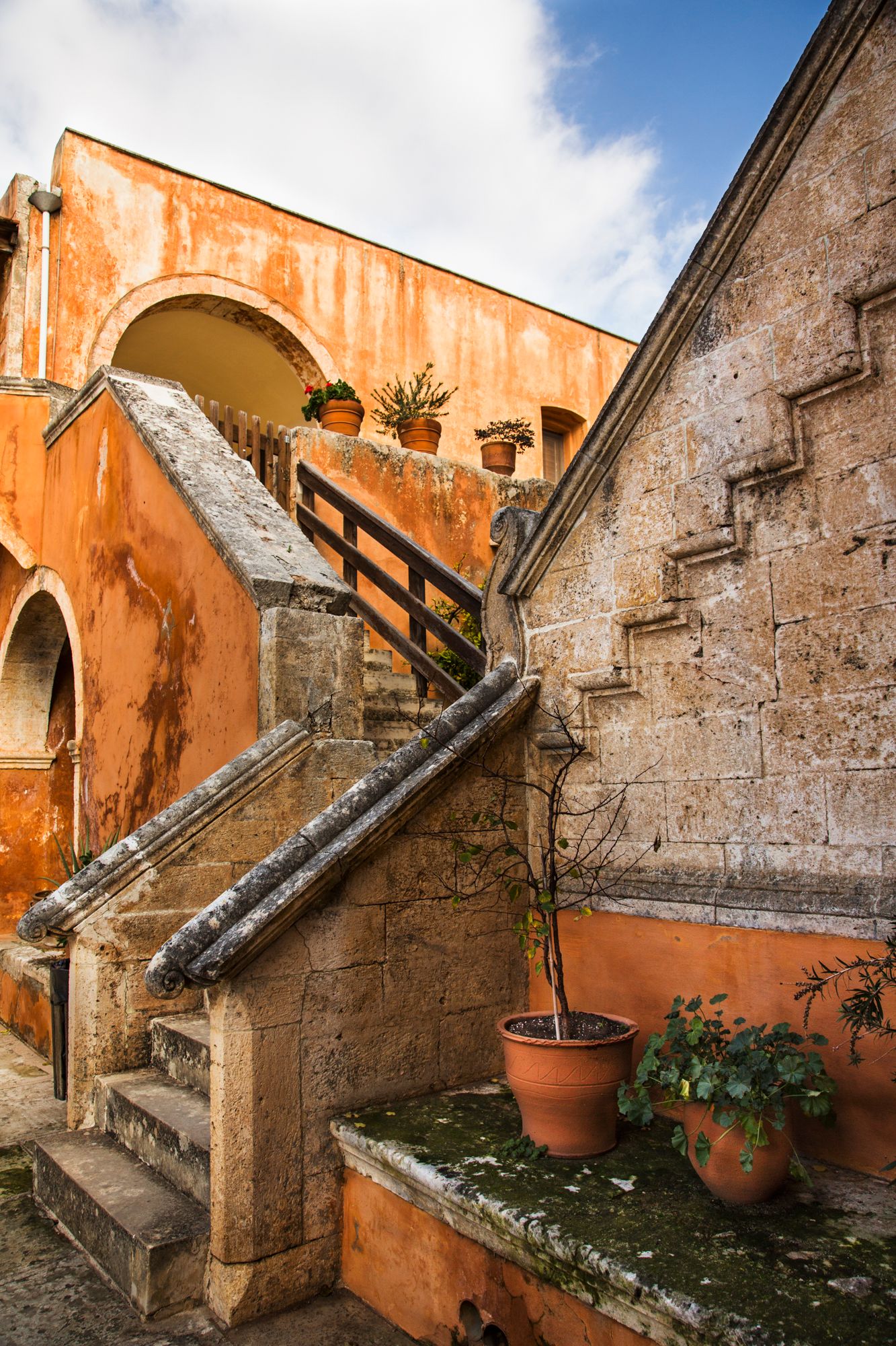 Ancient stone staircase with terracotta walls and potted plants in a Mediterranean monastery.