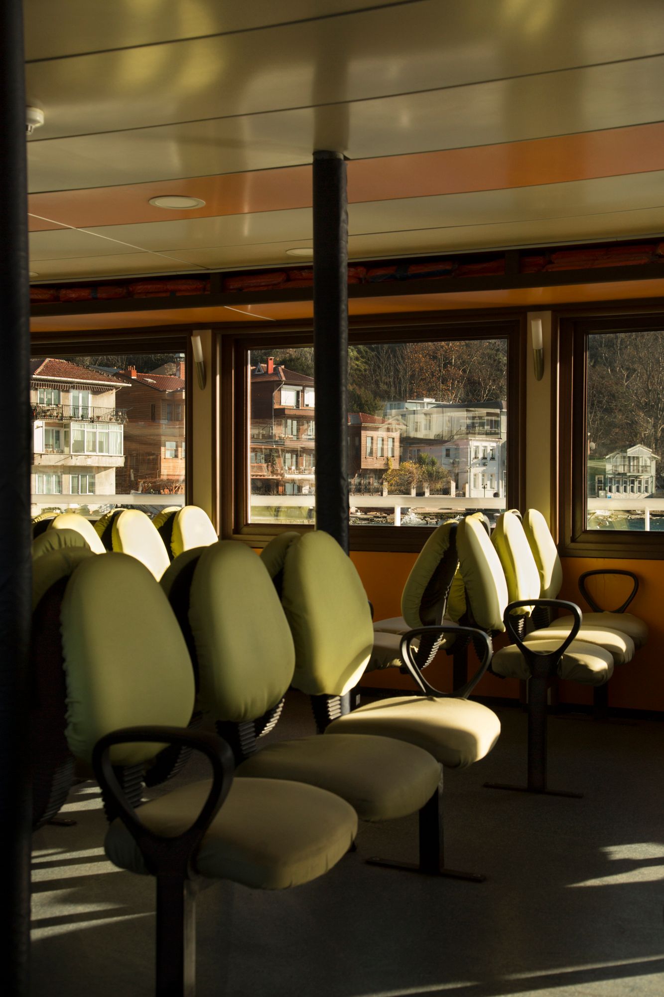 Empty passenger ferry interior with rows of cushioned seats and large windows.