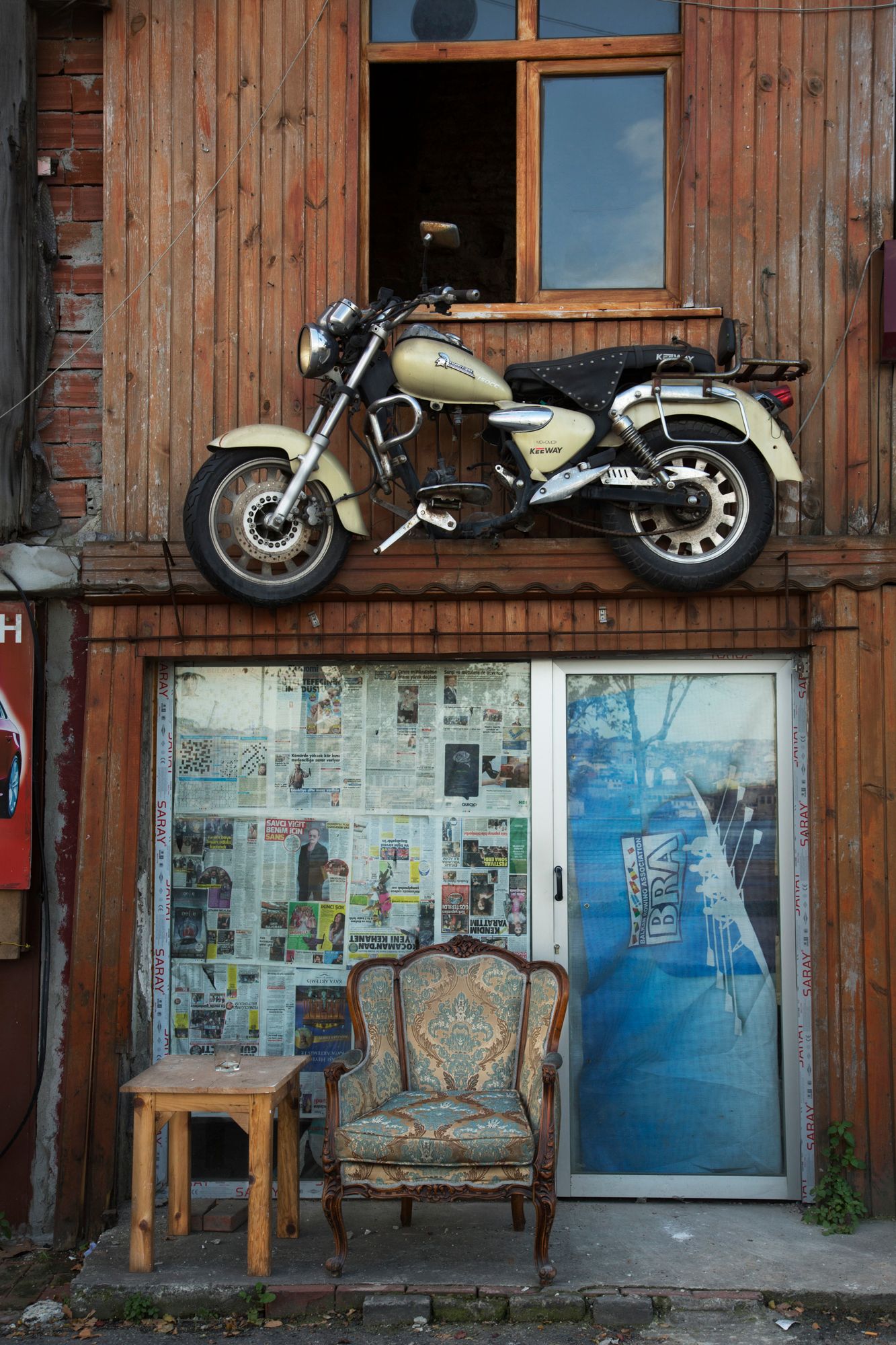 Vintage motorcycle mounted on wooden wall above antique chair and newspaper collage.