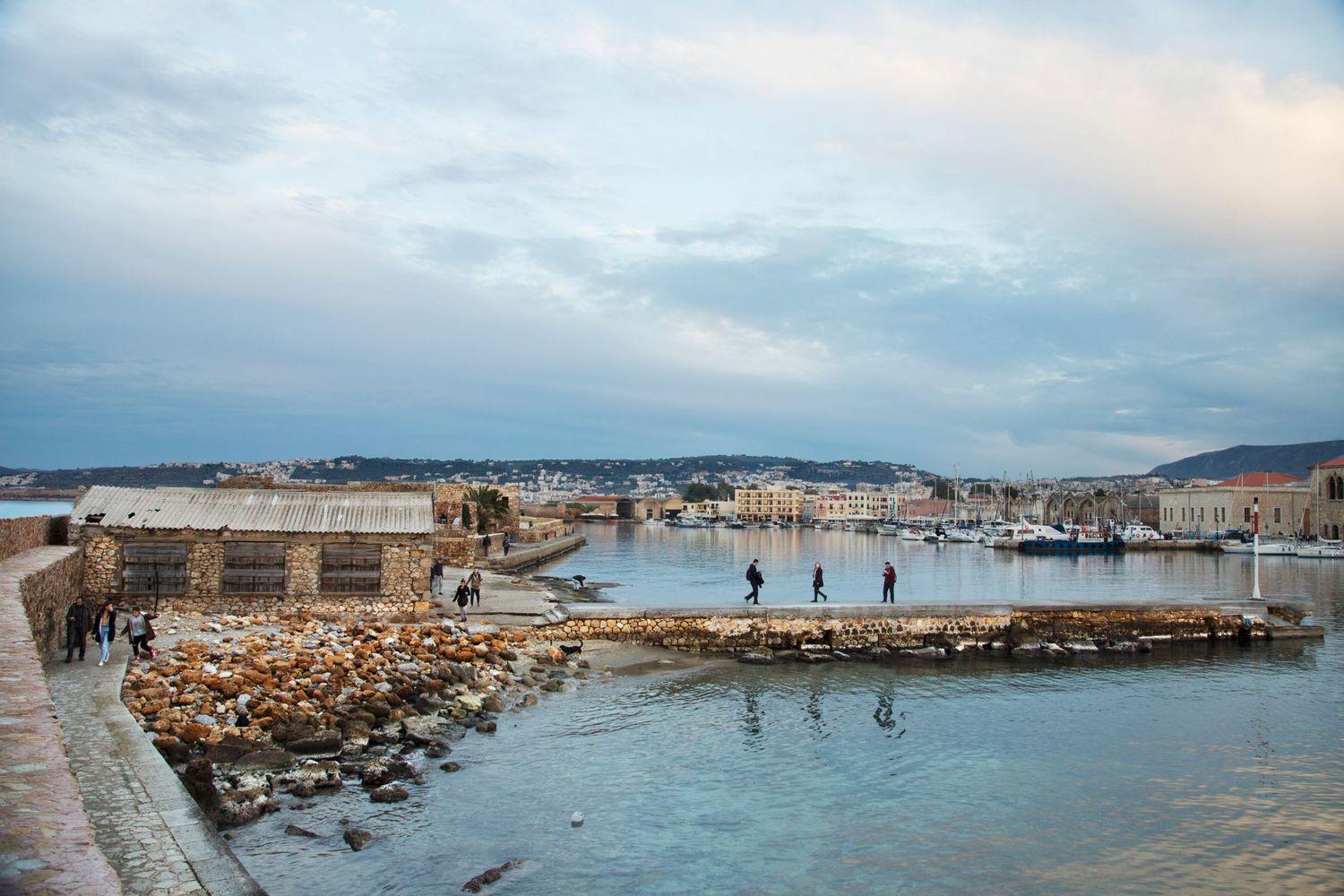 Stone pier and harbor with boats under cloudy sky in coastal town.