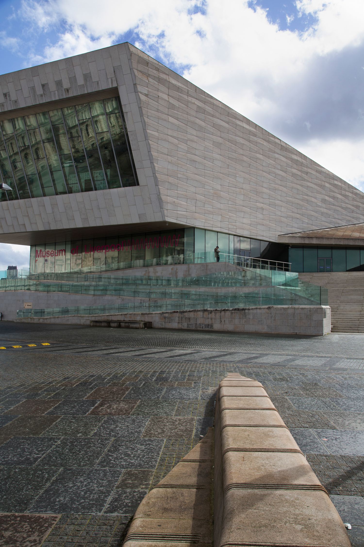 Modern angular white building with glass panels and geometric architecture on a wet stone plaza.