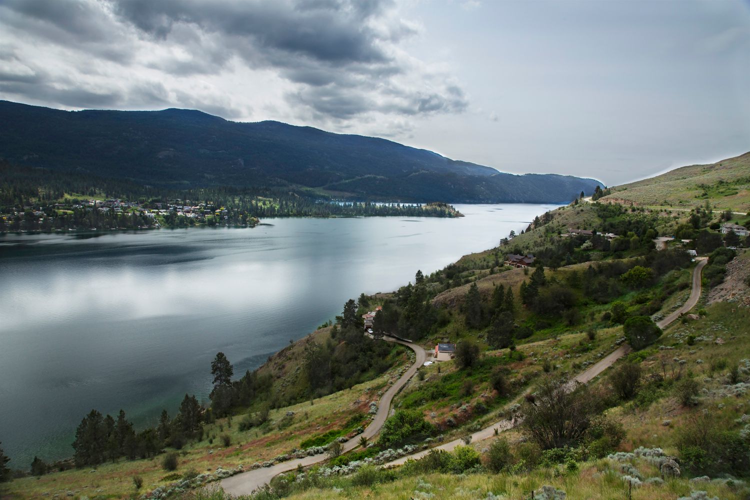 Scenic lake view with rolling hills and mountains under dramatic cloudy sky.