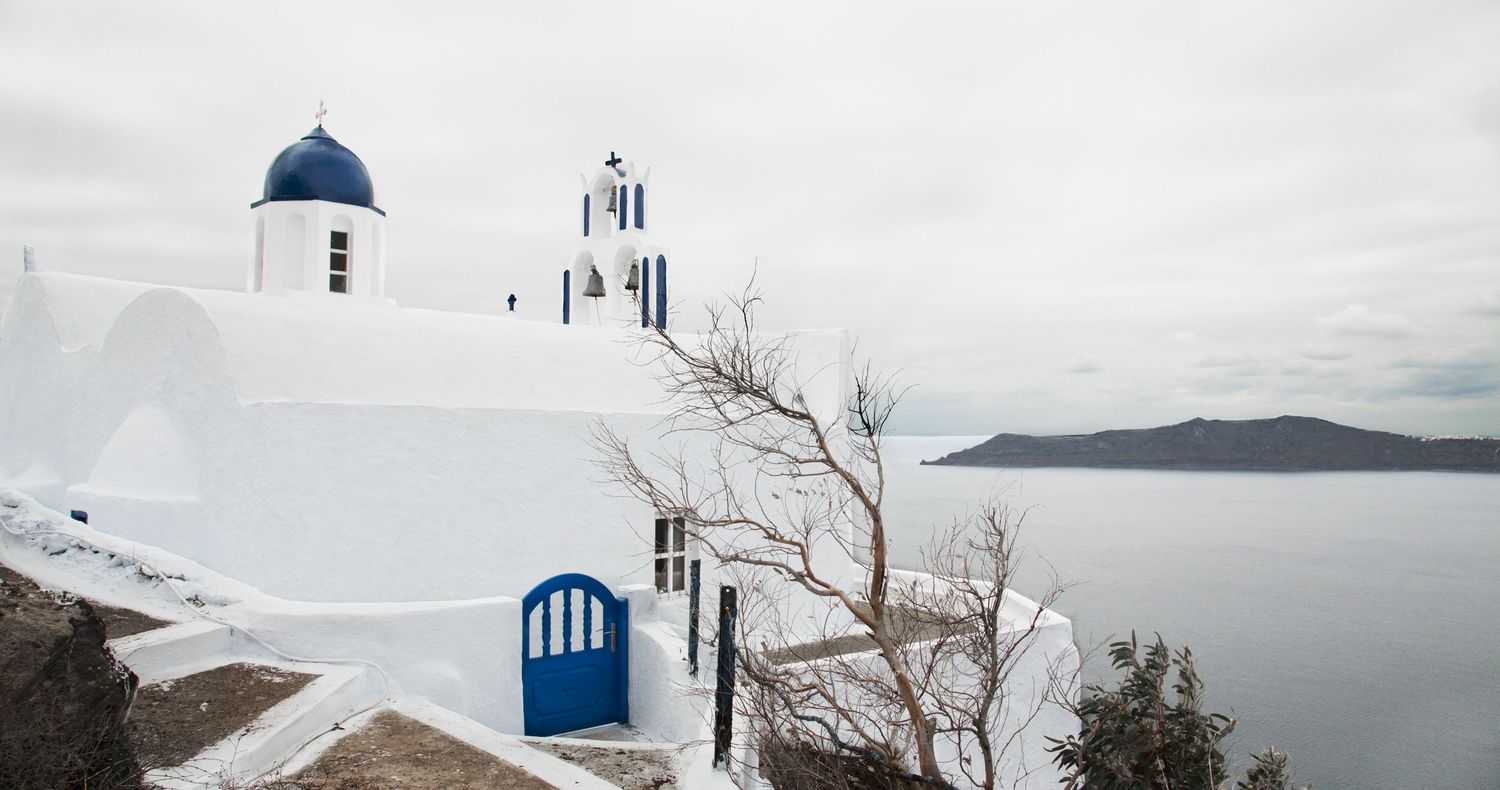 Traditional Greek church with blue dome against cloudy skies overlooking the Mediterranean Sea.