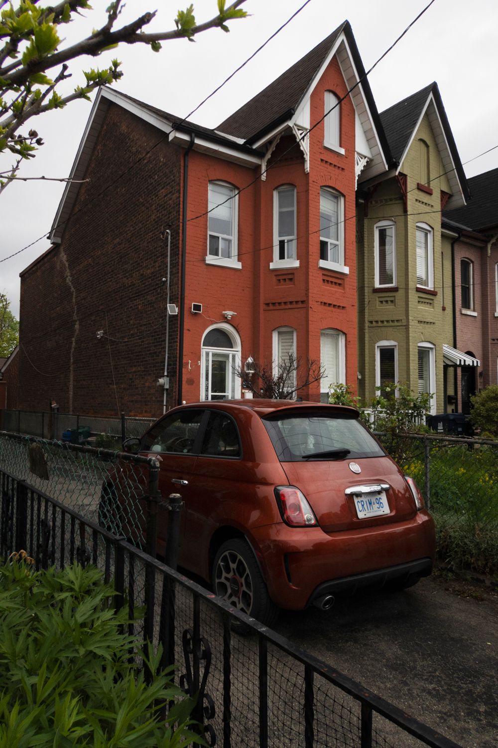 Row of colorful Victorian houses on a residential street with a red car parked in the driveway.