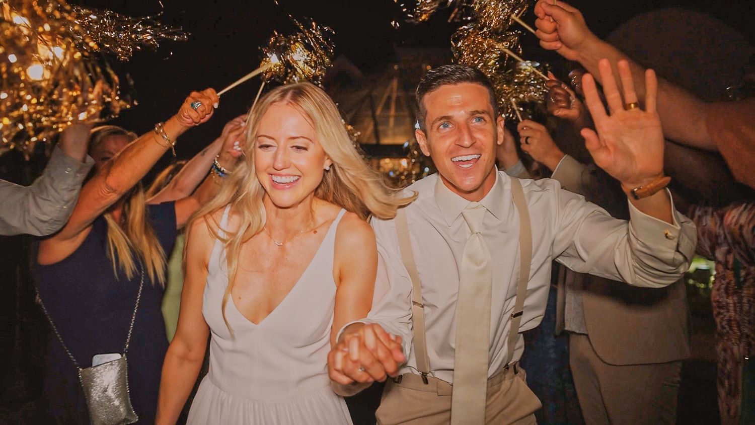 Happy newlyweds dancing and celebrating with guests on their wedding night under twinkling lights.