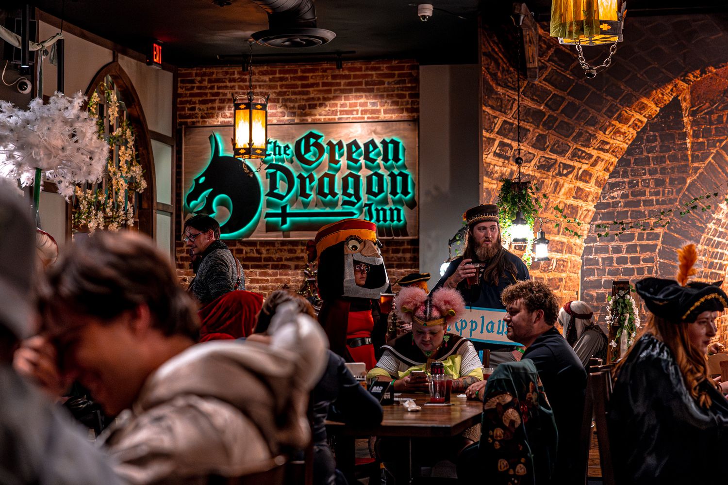 A crowded pub interior with exposed brick walls and neon Green Dragon Inn sign illuminated in the background.