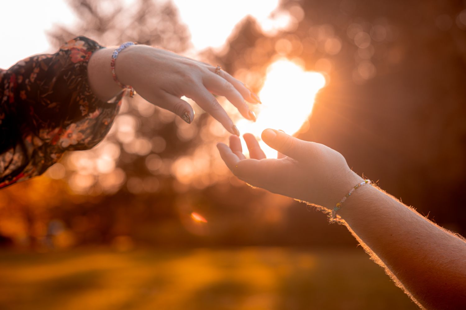 Two hands reaching towards each other with golden sunlight creating a dreamy bokeh effect in the background.