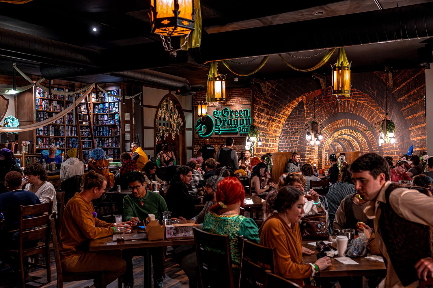 A dimly lit pub interior with hanging lanterns and patrons seated at tables.