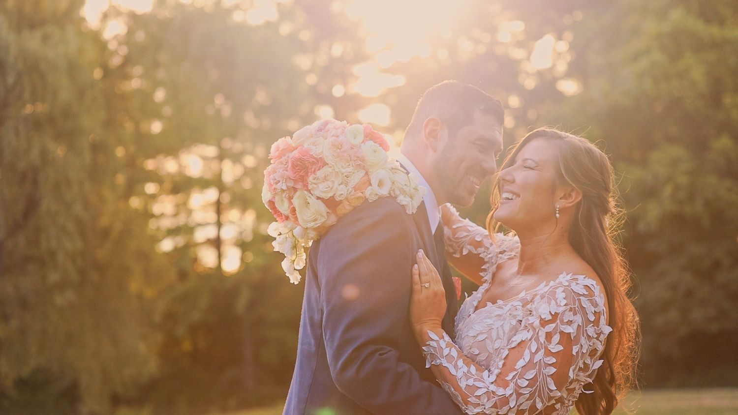 A couple shares a joyful moment in golden sunset light while wearing elegant wedding attire.