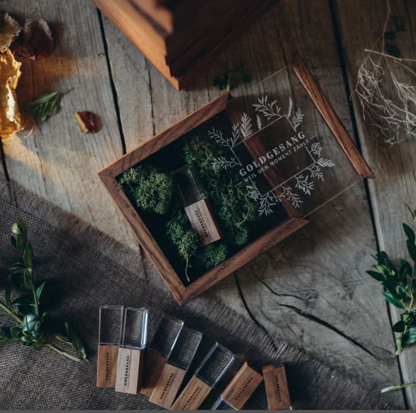 Essential oil bottles and wooden display box with greenery on a rustic wooden surface in moody lighting.