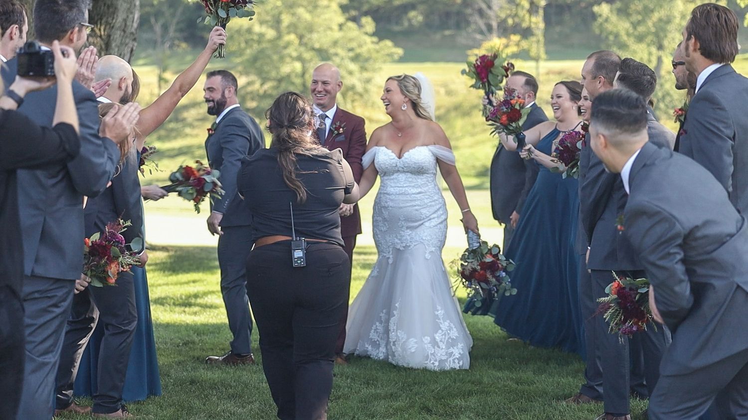 Wedding party in navy and white attire celebrates joyfully on sunny lawn during outdoor ceremony.