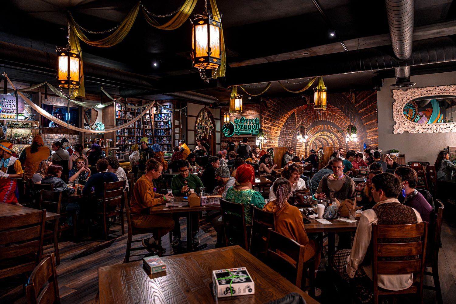 A crowded pub or restaurant interior with hanging lanterns and diners at wooden tables.