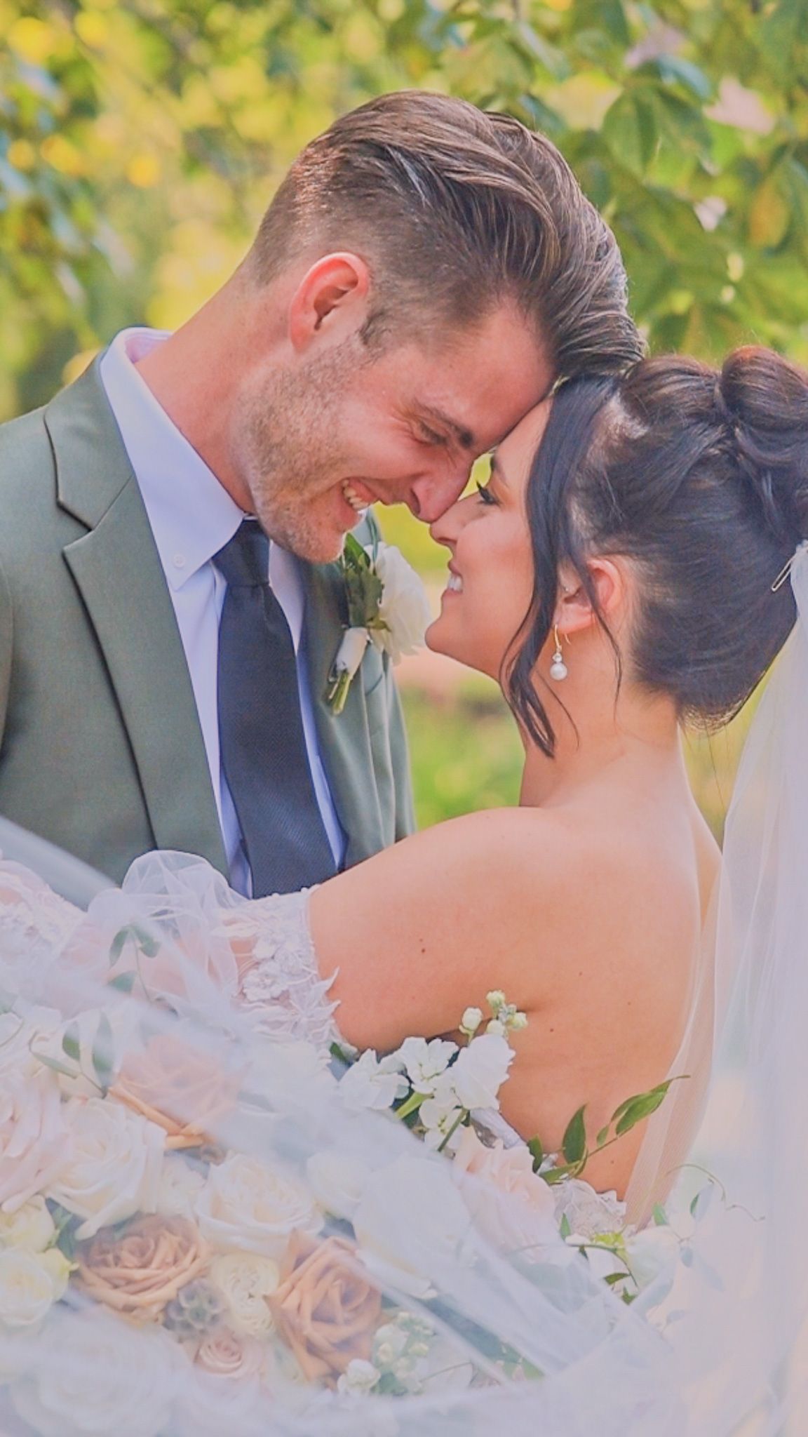 Newlywed couple shares intimate moment at outdoor wedding with soft natural lighting and floral bouquet details.