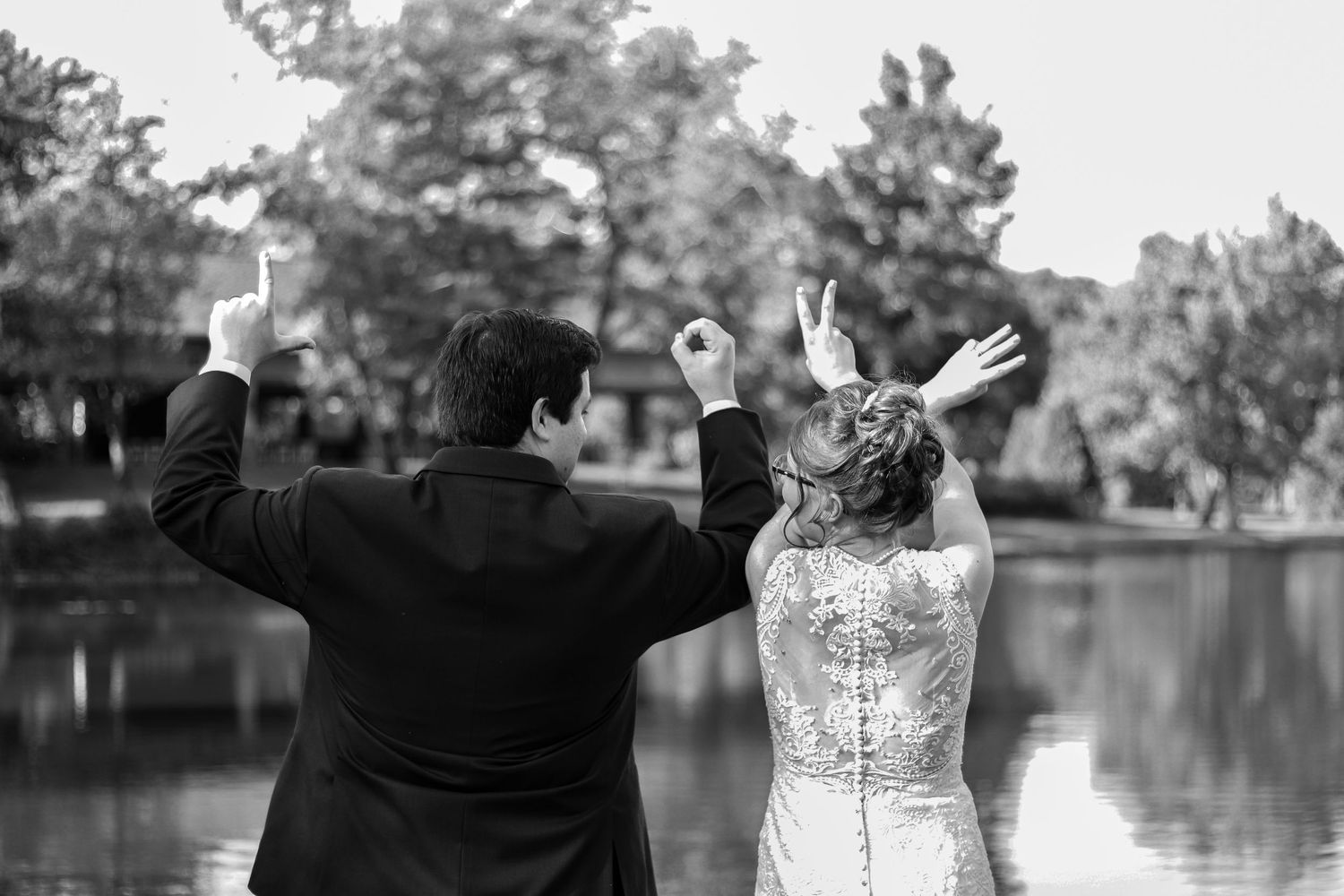 A joyful black and white photo of newlyweds raising their hands in celebration by a scenic lake.