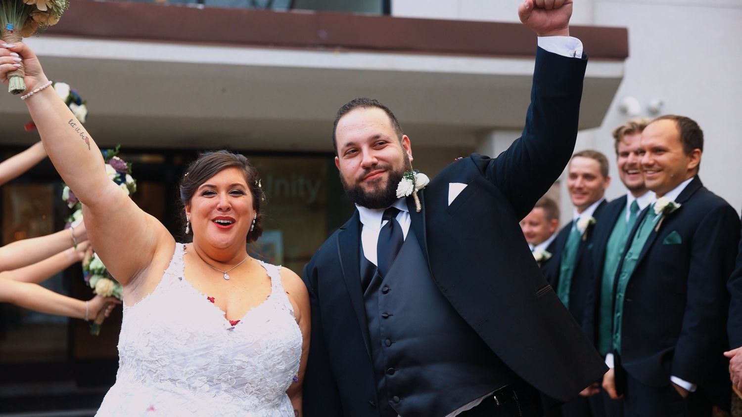 Joyful couple celebrates with raised arms during wedding ceremony while guests smile in background.