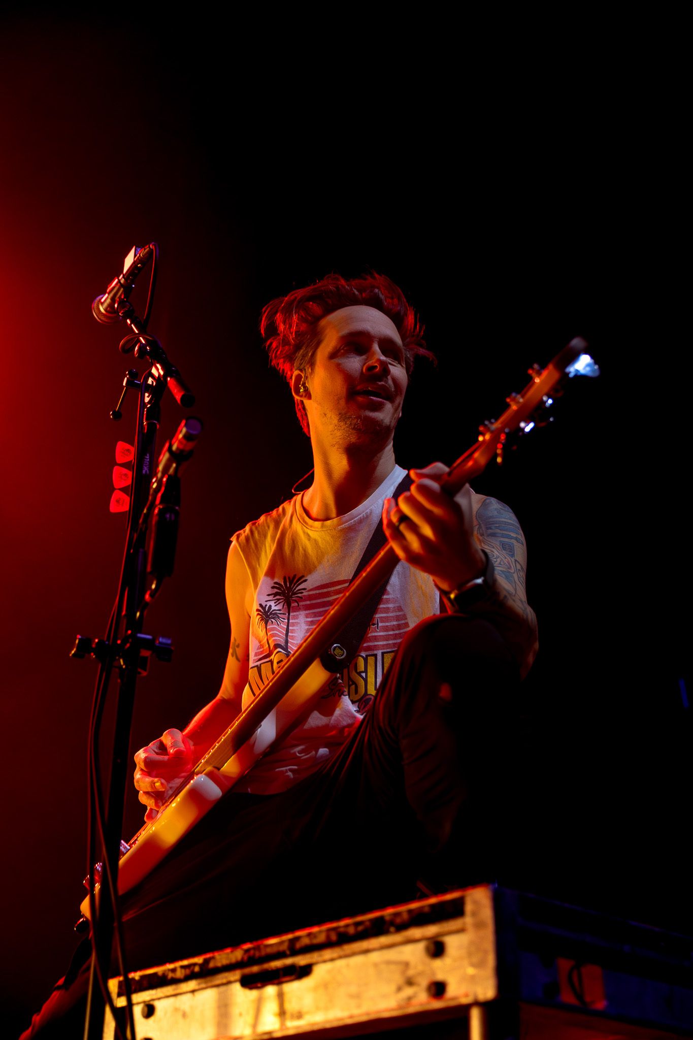A musician performs on stage with an electric guitar bathed in dramatic red lighting.