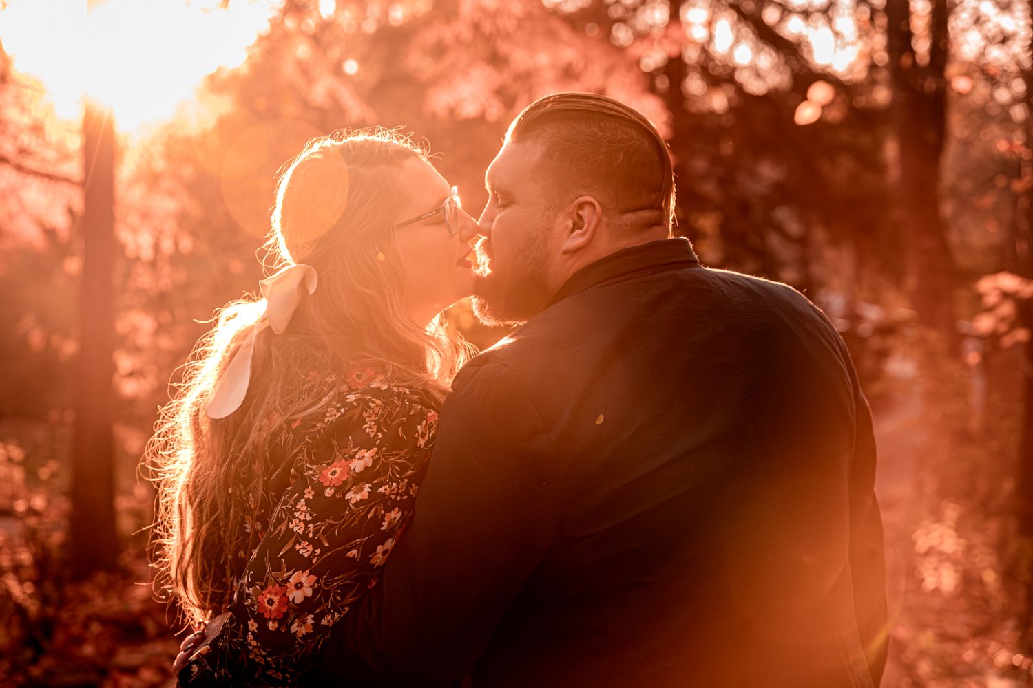 A romantic couple in silhouette shares a tender moment during golden hour in a sunlit forest setting.