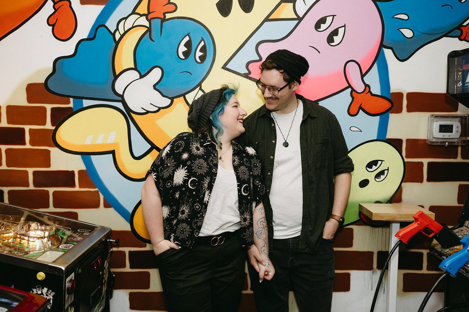 A couple shares a tender moment while standing in front of a colorful cartoon mural wall with playful characters.